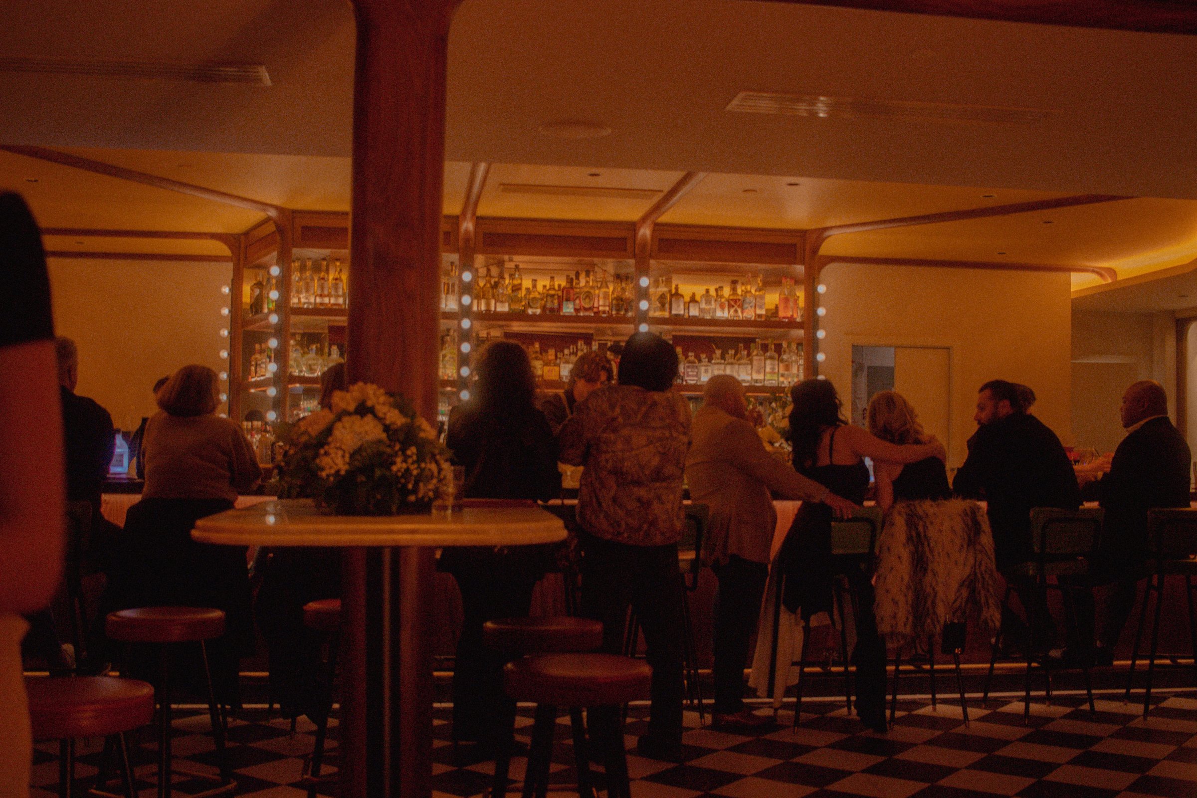 Atmospheric bar interior at The Red Room with patrons seated along the curved bar bathed in warm light and glowing liquor shelves
